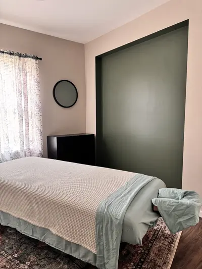 Massage table beside a curtained window and green accent wall at D2H Wellness